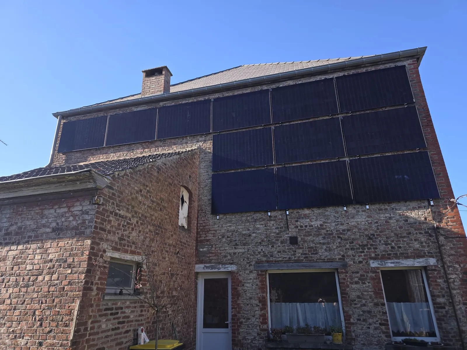 Panneaux photovoltaïques posés verticalement en façade d’une bâtisse en briques.